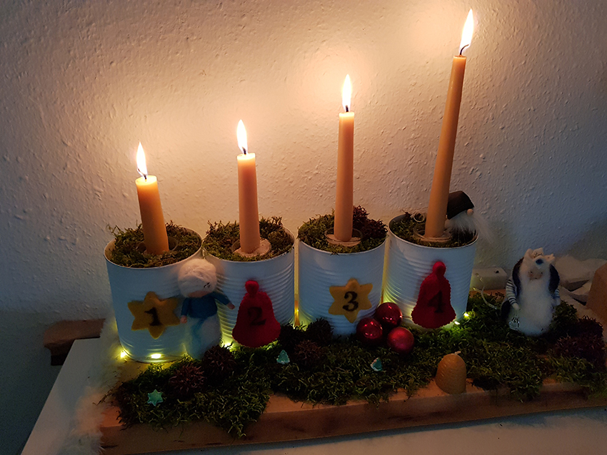 Ein Adventskranz mit Konservendosen, auf dem alle vier Kerzen brennen.