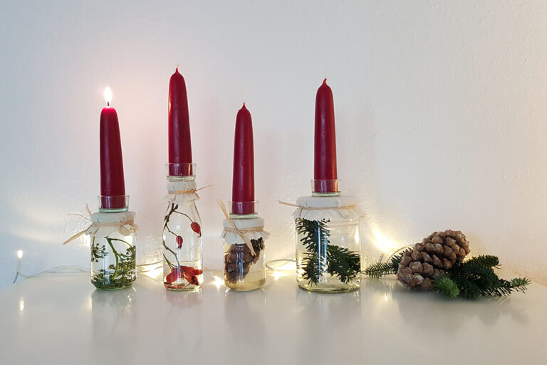 Einen Adventskranz basteln kann man auch mit Gläser, die mit Naturmaterialien gefüllt und mit Kerzen geschmückt sind.