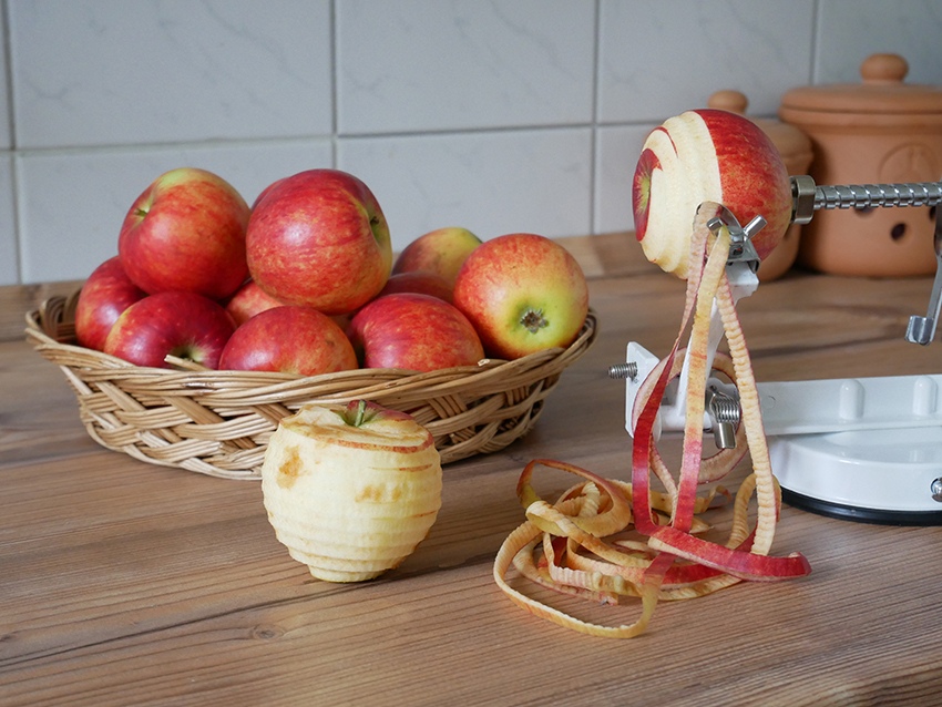 EIne Apfelschälmaschine steht auf dem Tisch und schält einen Apfel.