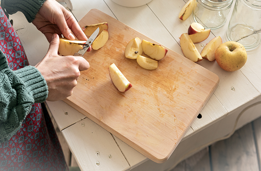 Äpfel werden auf einem Holzbrett mit einem Messer in Scheiben geschnitten und entkernt.