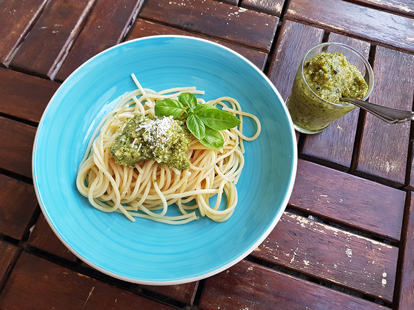 Die Spaghetti auf dem blauen Teller sind mit dem grünen Zucchini-Pesto und einem Basilikumblatt sowie Parmesan gekrönt.