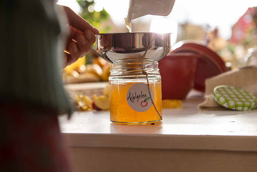 Selbst gemachtes Apfelgelee wird durch einen Trichter in ein beschriftetes Glas gefüllt.