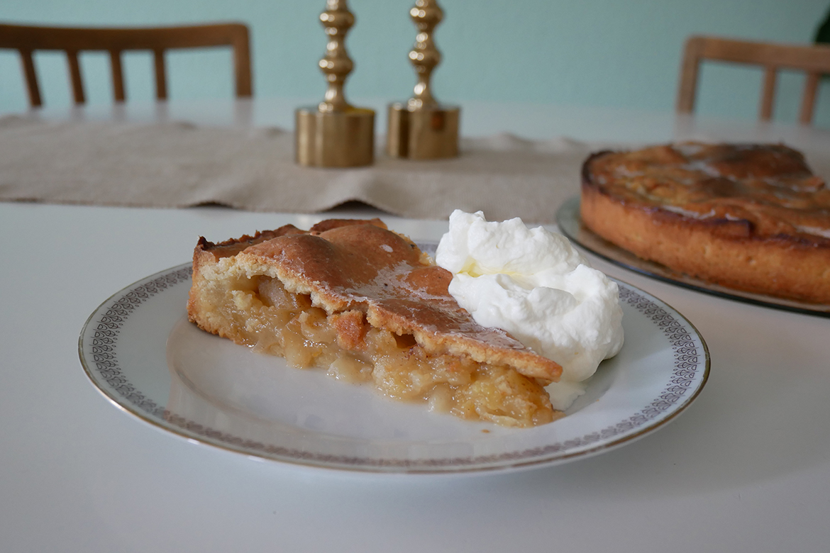 Ein Stück Apfelkuchen mit einer Portion Sahne steht auf dem Tisch bereit.