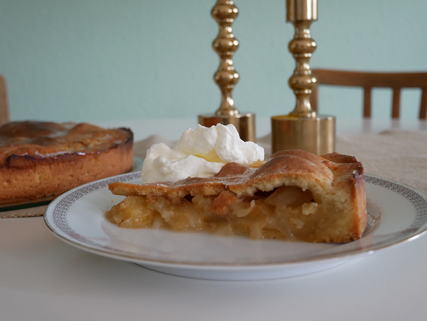Ein Stück Apfelkuchen auf einem Teller steht auf dem Tisch bereit.