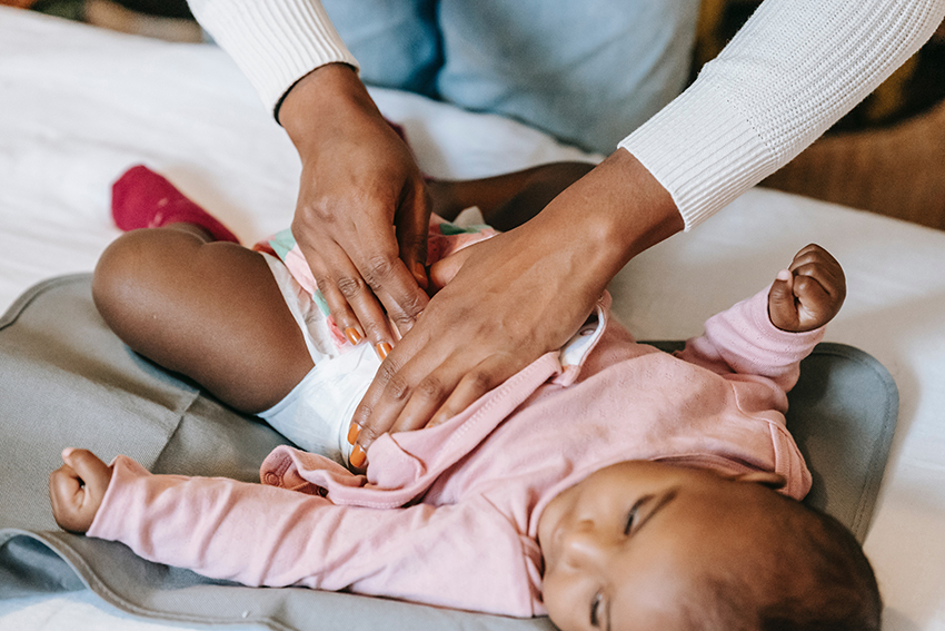 Ein Baby liegt auf einem Wickeltisch, seine Mutter verschließt eine konventionelle Windel.