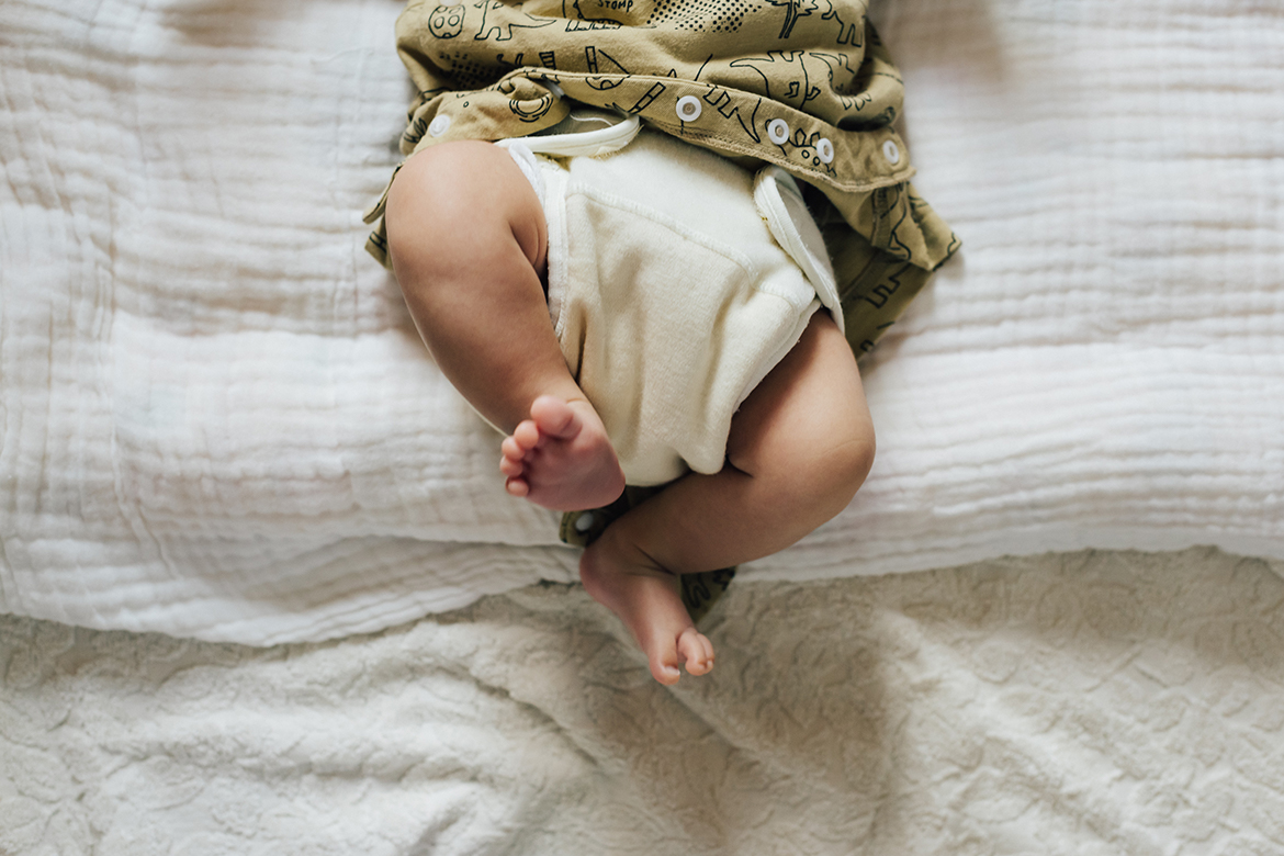 Ein Baby liegt auf einer weißen Unterlage und trägt eine helle Stoffwindel.