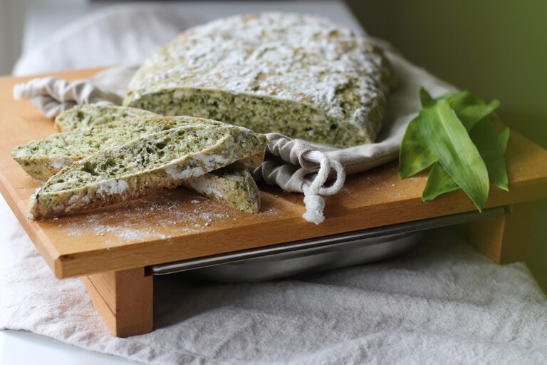 Das Bärlauchbrot liegt angeschnitten auf einem Schneidebrett aus Holz.