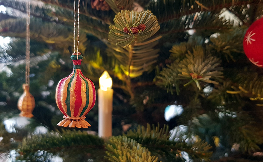 Eine bunt bemalte Mohnkapsel hängt als Baumschmuck am Weihnachtsbaum.