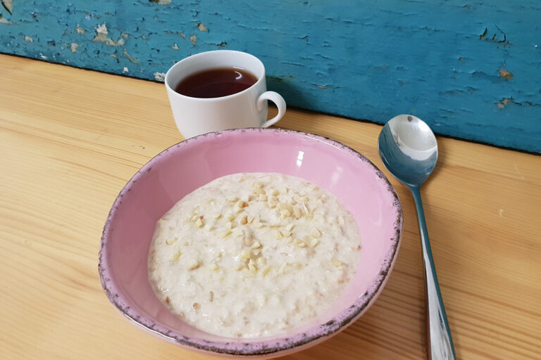 Eine Schüssel Birchermüsli steht neben einer Tasse Tee und einem Löffel.