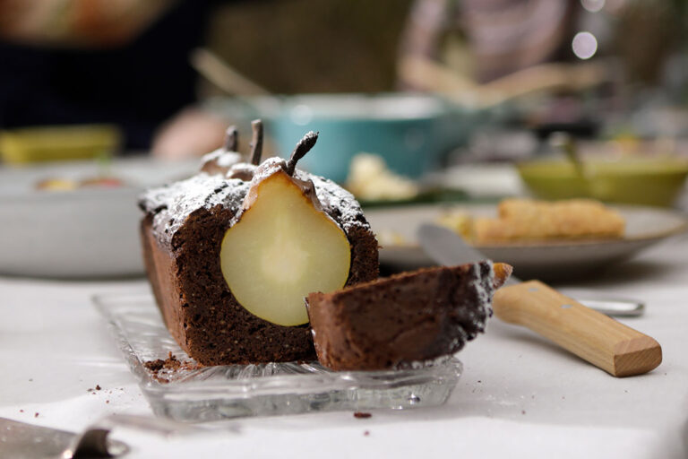 Ein Rotweinkuchen mit versunkenen Birnen steht angeschnitten auf einem gedeckten Tisch.