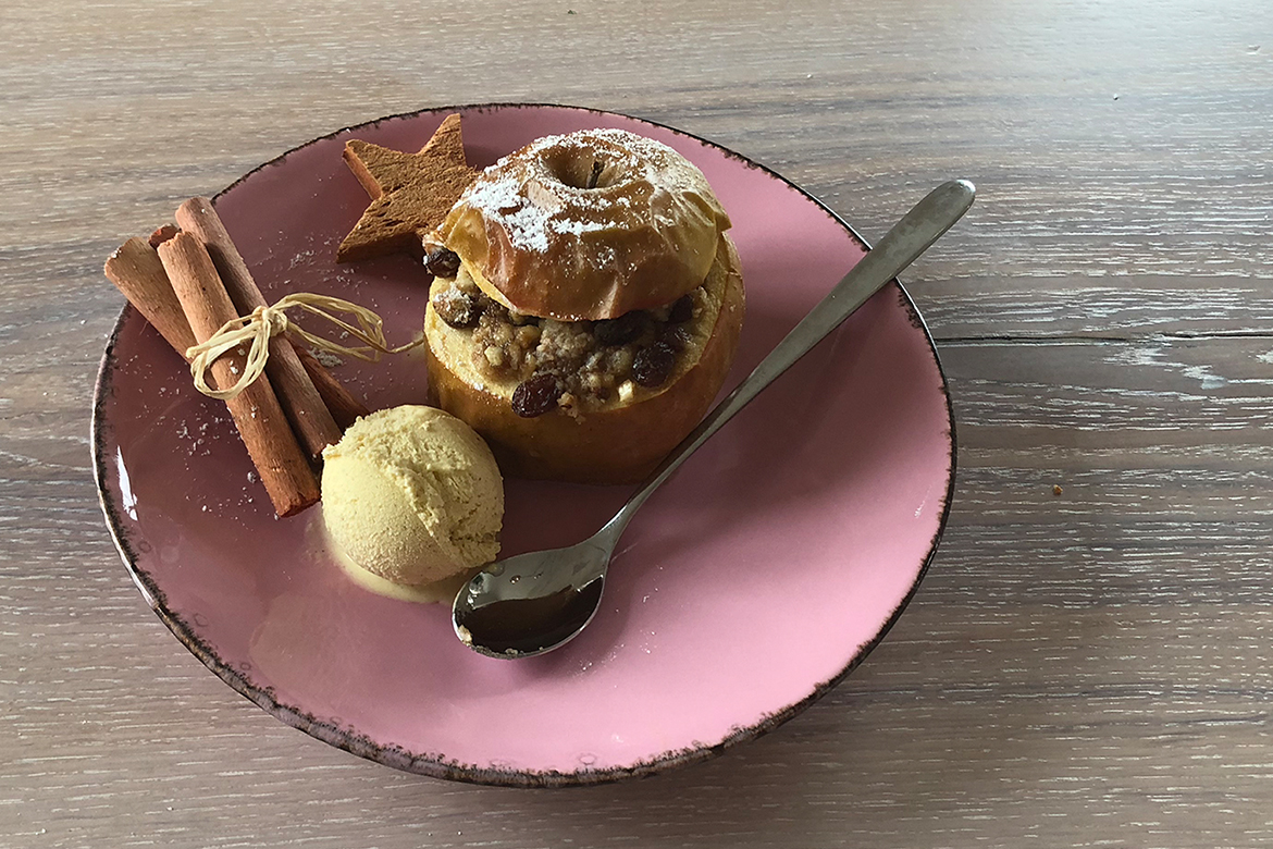 Ein Bratapfel ist mit einer Kugel Eis auf einen rosa Teller angerichtet.