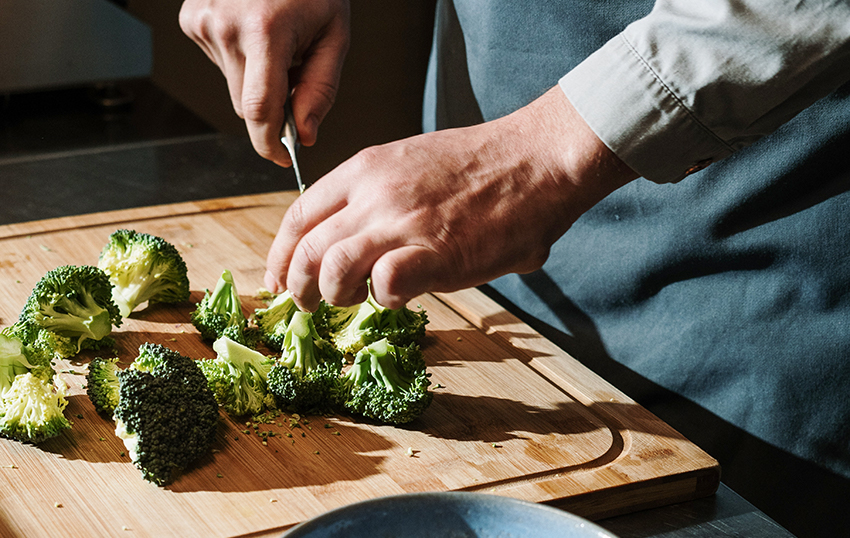 De broccoli wordt op een houten plank met een mes in kleine stukjes gesneden.
