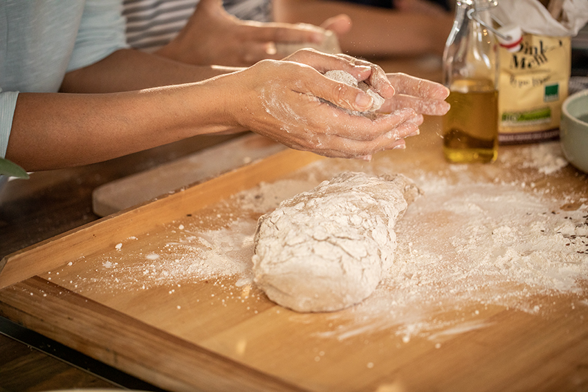 Frau knetet und formt beim Brotbacken einen bemehlten Brotteig auf einem Holzbrett.