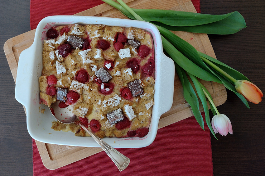 Der Brotpudding steht in einer Auflaufform auf einem Holzbrett, auf dem zwei Tulpen liegen.