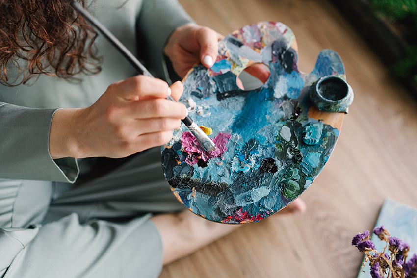 Ein Pinsel wird in Farbe auf einer bunten Palette getunkt.