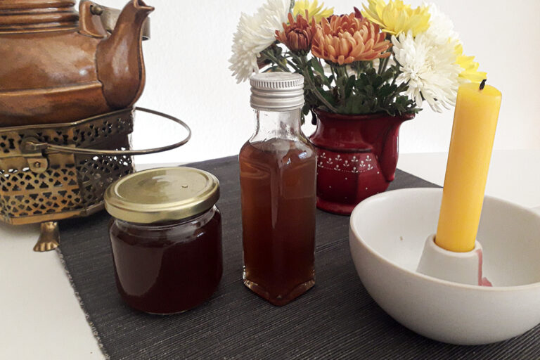 Der selbst gemachte Chai-Sirup steht in Gläschen abgefüllt neben einer Kerze und einem Teekessel auf dem Tisch.