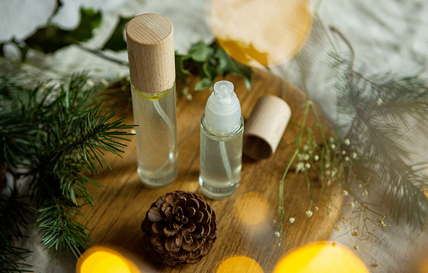 De zelfgemaakte deodorantspray staat in twee flesjes op een houten plank met kerstversiering.