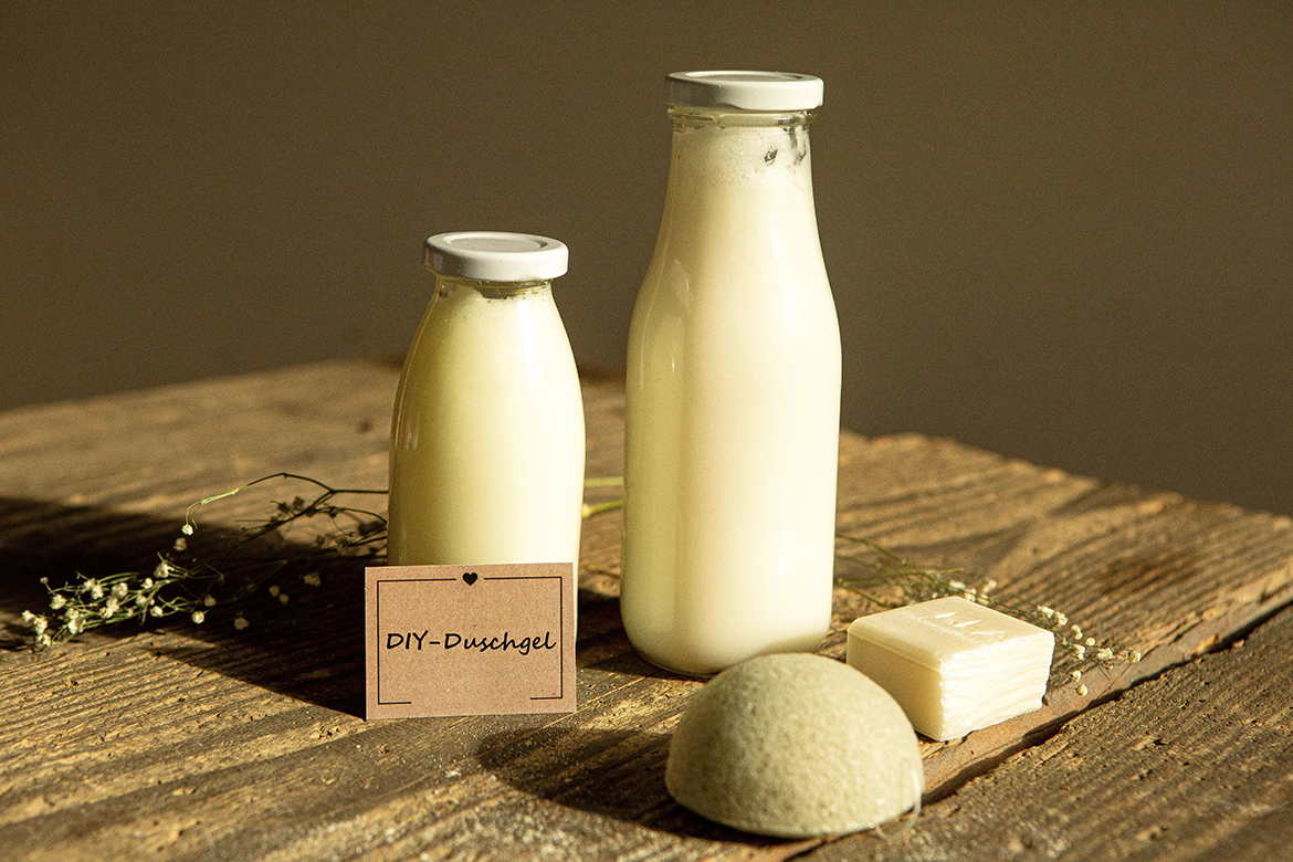 Zwei Flaschen selbst gemachtes Duschgel stehen auf einem Holztisch, an der kleinen Flasche lehnt ein beschriftetes Etikett.