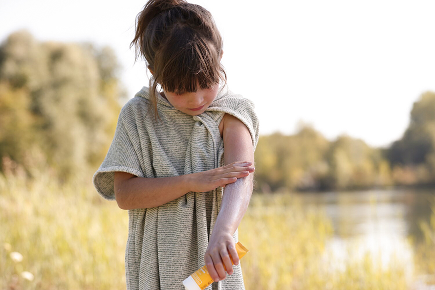 Ein kleines Mädchen cremt sich die Arme mit Sonnenschutz ein.