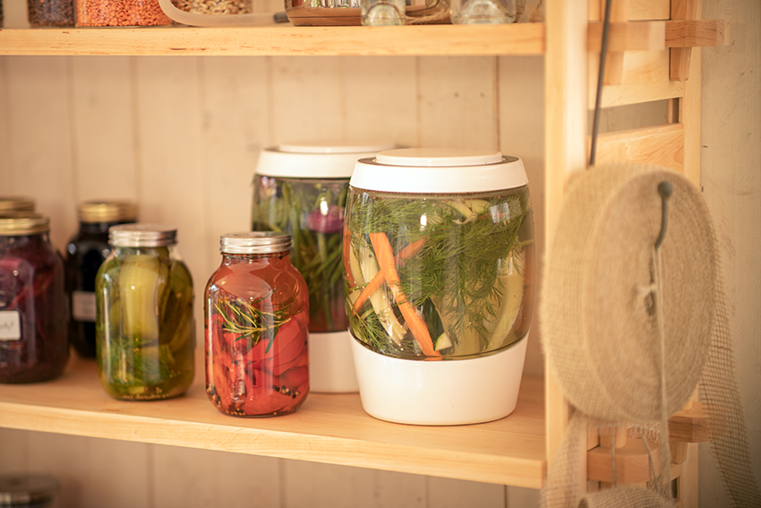 Gläser mit eingemachtem und fermentiertem Gemüse stehen in einem Holzregal.
