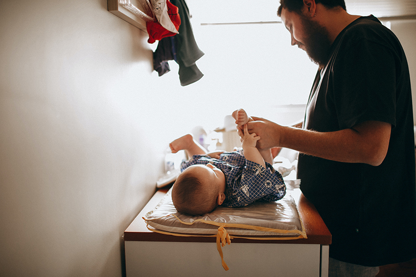 Ein Erzieher wechselt einem Baby die Windel, das Baby liegt auf einem Wickeltisch.