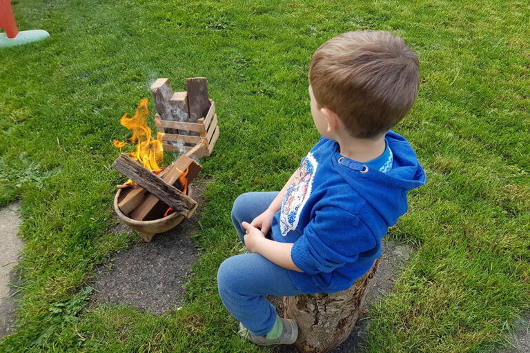 Der kleine Junge sitzt neben einem kleinen Feuerchen.