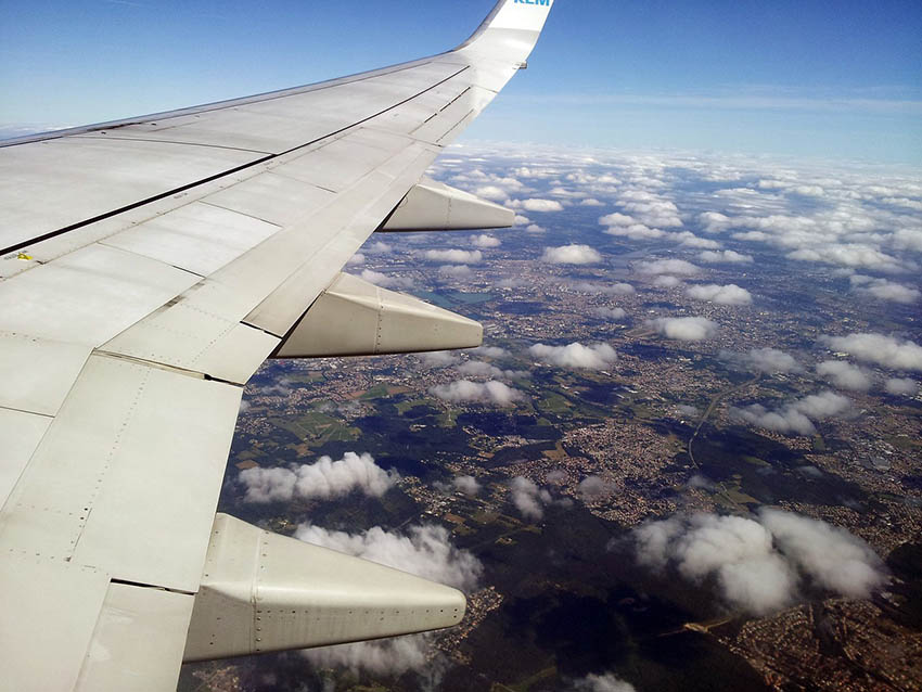 Flugzeugflügel mit Blick auf Wolken und die tiefliegende Landschaft.