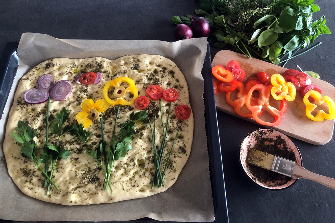 Ein selbst gemachtes Focaccia ist mit Gemüse in Blumenform belegt.