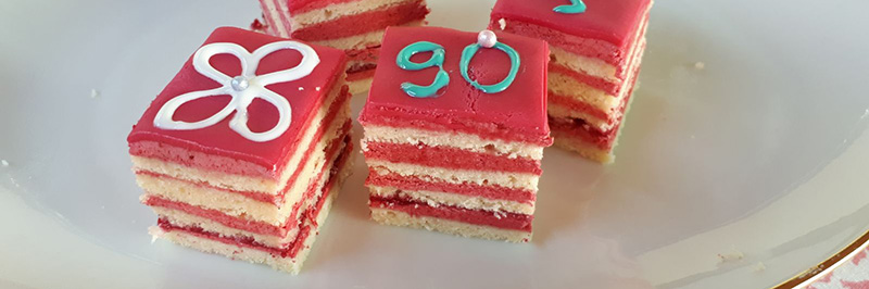 Zwei mit pinker Füllung geschichtete Petit four mit bemalter Fondant-Decke.