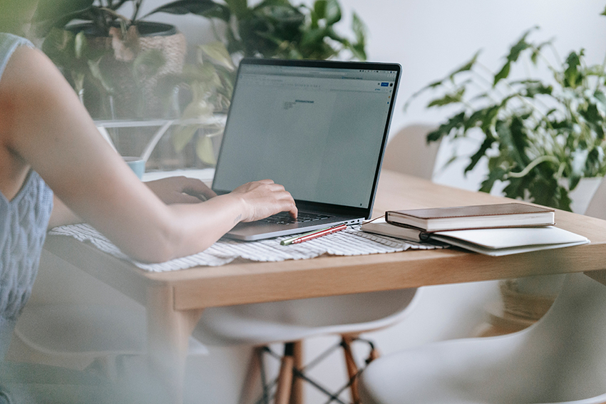 Frau sitzt an einem Tisch und arbeitet konzentriert im Homeoffice an ihrem Laptop.