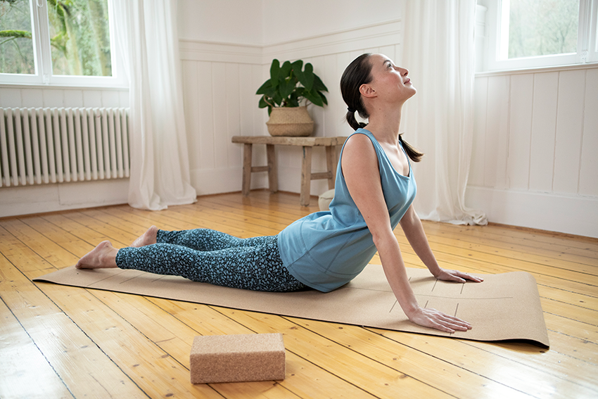 Frau führt eine Yogaübungen mit dem Namen Kobra auf einer Yogamatte aus Kork durch.