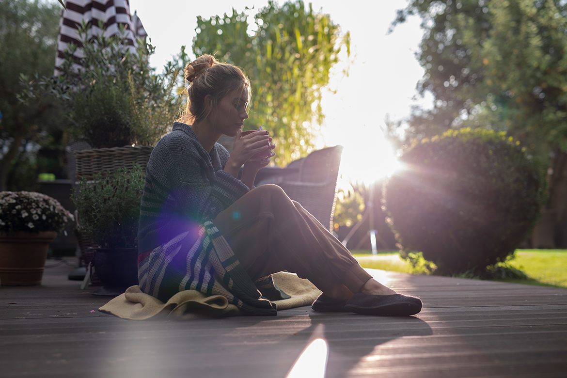 Eine Frau sitzt mit einer Tasse in der Hand auf ihrer Terrasse und genießt die Stille.