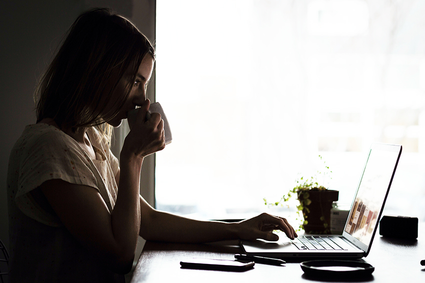 Frau sitzt an ihrem Laptop und trinkt zeitgleich Kaffee für konzentriertes Arbeiten im Homeoffice.