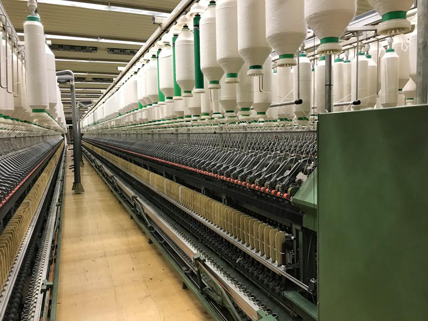 Eine lange Halle, in der Textilgarn auf Spulen von der Decke hängt.