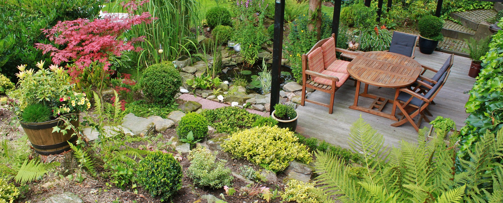 Der abschüssige Garten führt auf eine Holzterrasse an einem kleinen Gartenteich.