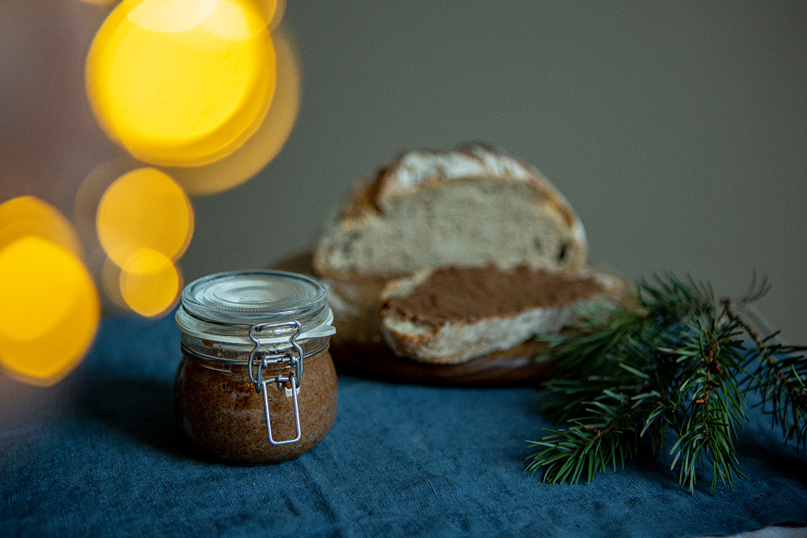 Der Gebrannte-Mandeln-Aufstrich steht in einem Gläschen vor einem Brett mit bestrichenem Brot darauf.