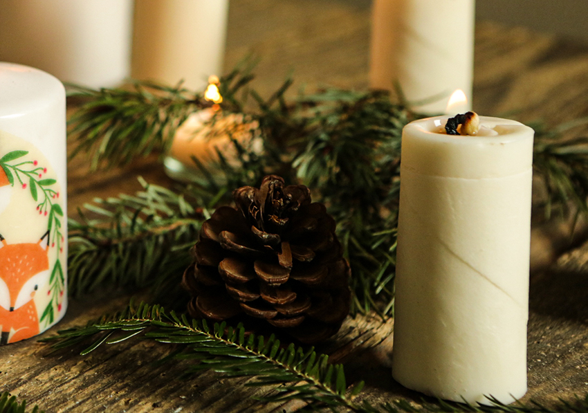 Zelfgemaakte kaarsen staan op een kerstversierde houten tafel.