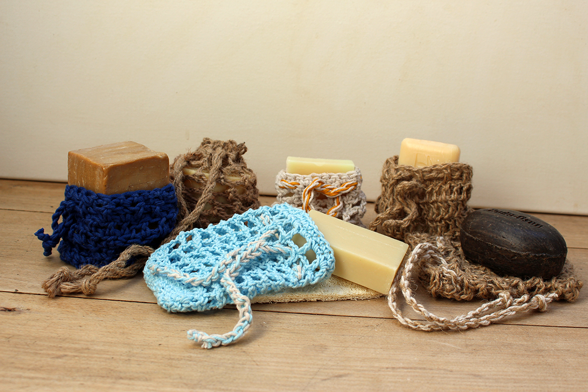 Gehäkelte Seifensäckchen und Seifenstücke liegen auf einer Holzoberfläche.