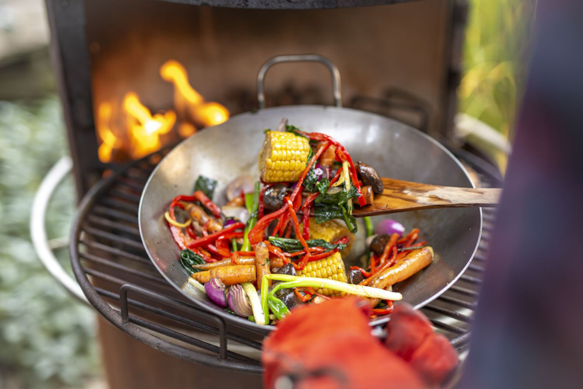 Gemüse wird auf dem Grill in einer Pfanne gegart.