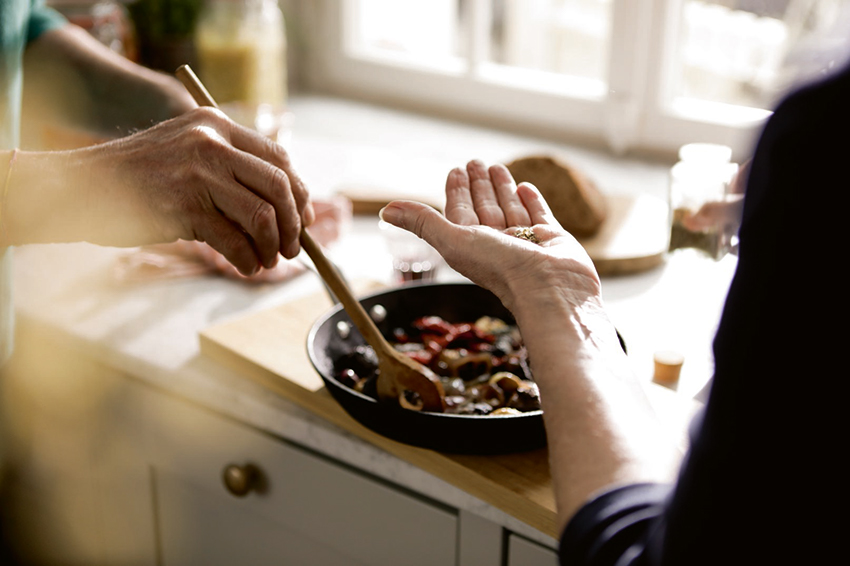 Eine Pfanne mit Gemüse wird für das Garen vorbereitet, die Gewürze in der Hand werden gleich hinzugegeben.