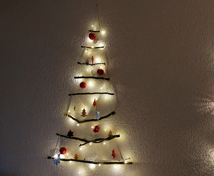 Der Weihnachtsbaum aus Ästen ist mit einer Lichterkette geschmückt.