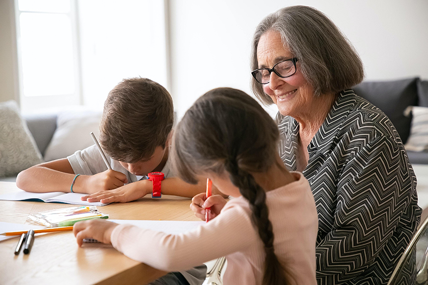 Eine Rentnerin sitzt ein einem Mehrgenerationenhaus mit zwei Kindern zusammen, die malen.