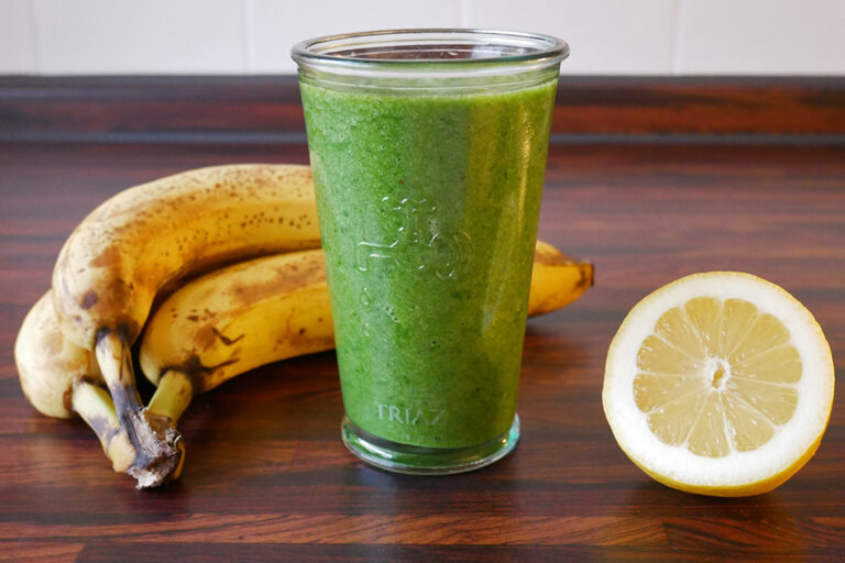 Ein Glas grüner Smoothie mit Bananen und Zitrone dekoriert.