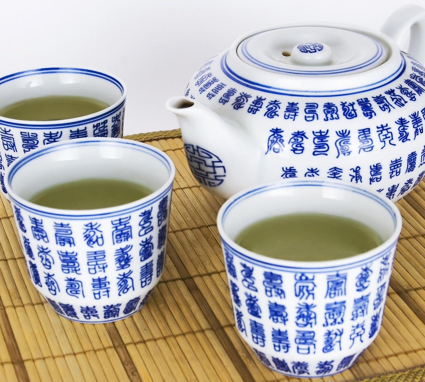 Drei asiatische Teebecher mit Grünem Tee stehen neben einer Teekanne.