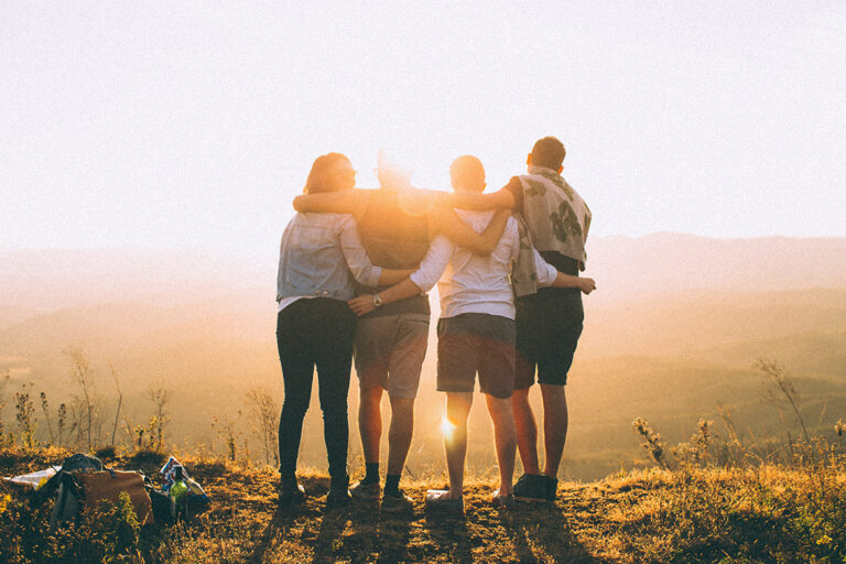 Eine Gruppe Menschen hält sich in den Armen und schaut gemeinsam den Sonnenuntergang an.