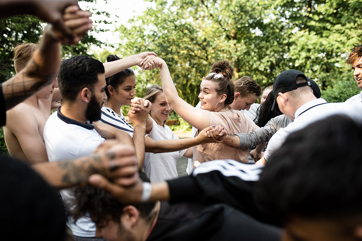 Eine Gruppe junger Menschen bildet im Rahmen eines Kurses der MUT Academy einen Kreis, um sich gegenseitig zu unterstützen.