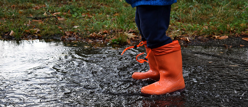 Orangene Gummistiefel, die an den Füßen eines Kindes in eine Pfütze springen.