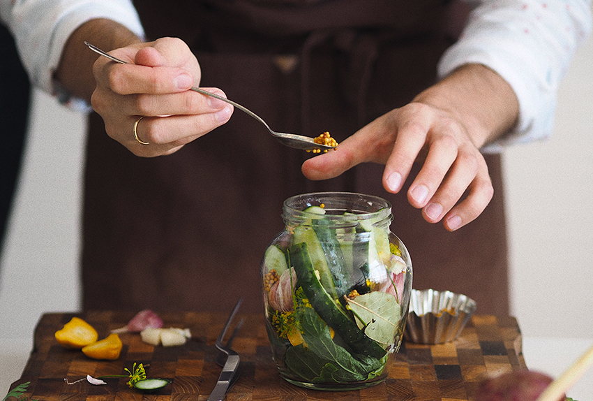 Op de seizoenskalender van juni staan augurken, hier ingemaakt met mosterd en kruiden in een glazen potje.