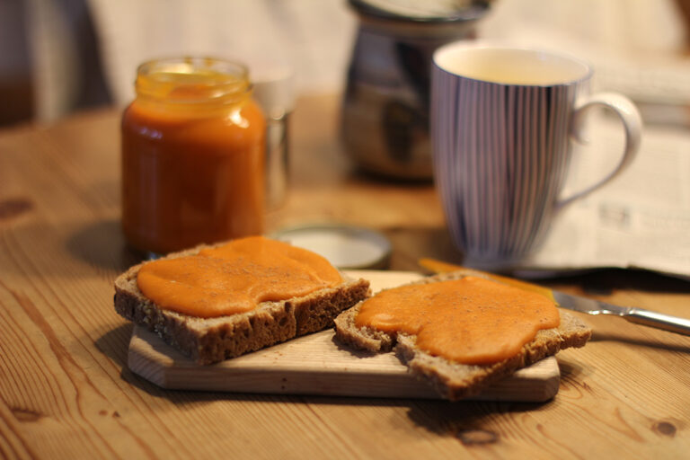 Zwei Scheiben Brot sind mit Kürbismarmelade bestrichen und liegen auf einem Schneidebrettchen.