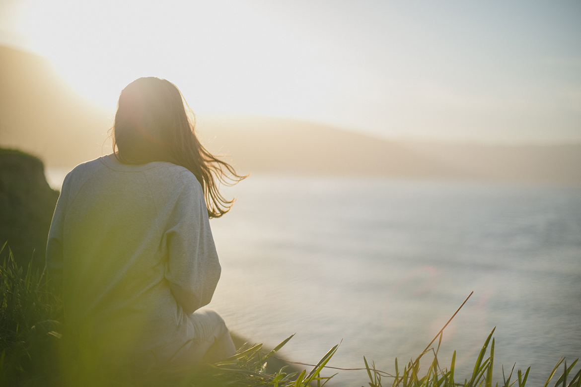 Eine Frau mit Hochsensibilität sitzt auf einer Klippe am Meer und genießt die Stille.
